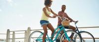 two people riding bikes near the beach on a sunny day